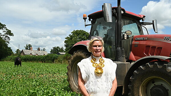 Rachel Gilmour MP stood in a green field with a red tractor behind her, smiling